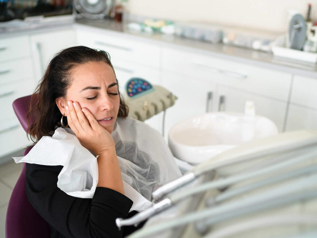 Stock photo of a dental patient in pain, holding the side of her face.