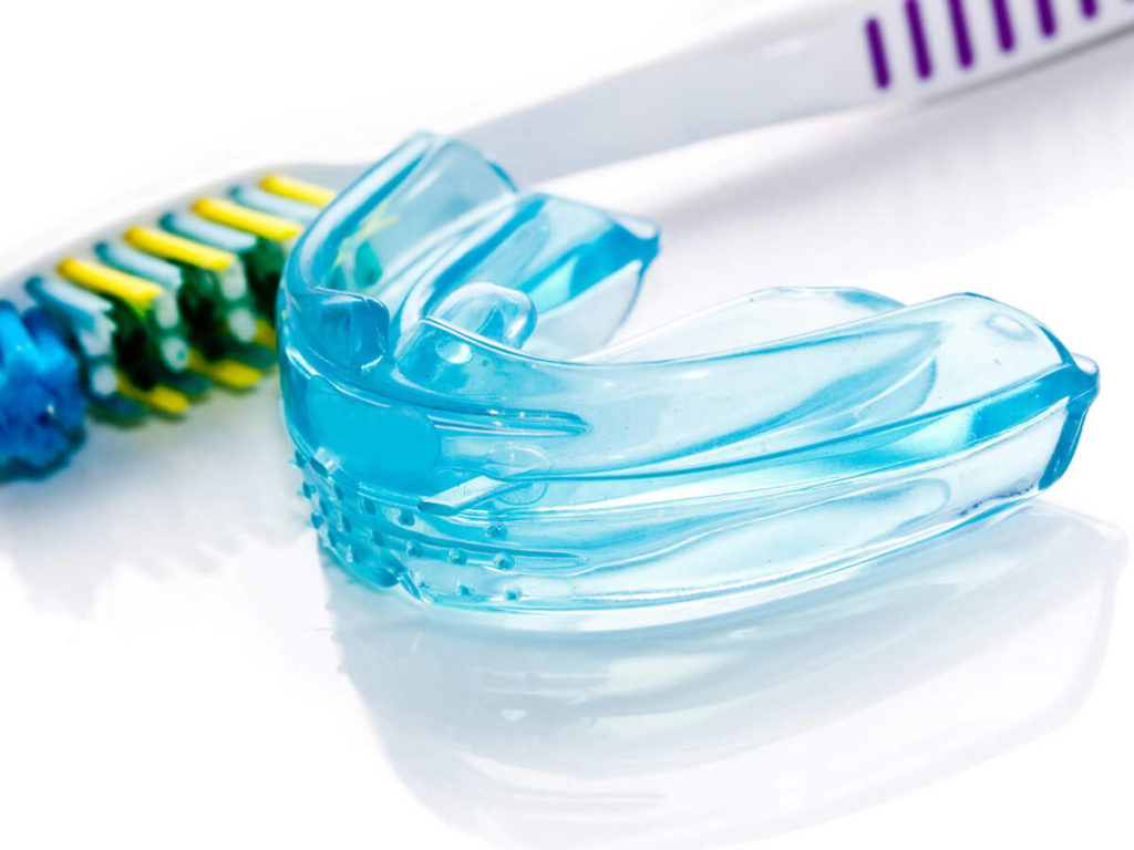 Photo of a blue plastic mouthguard next to a toothbrush