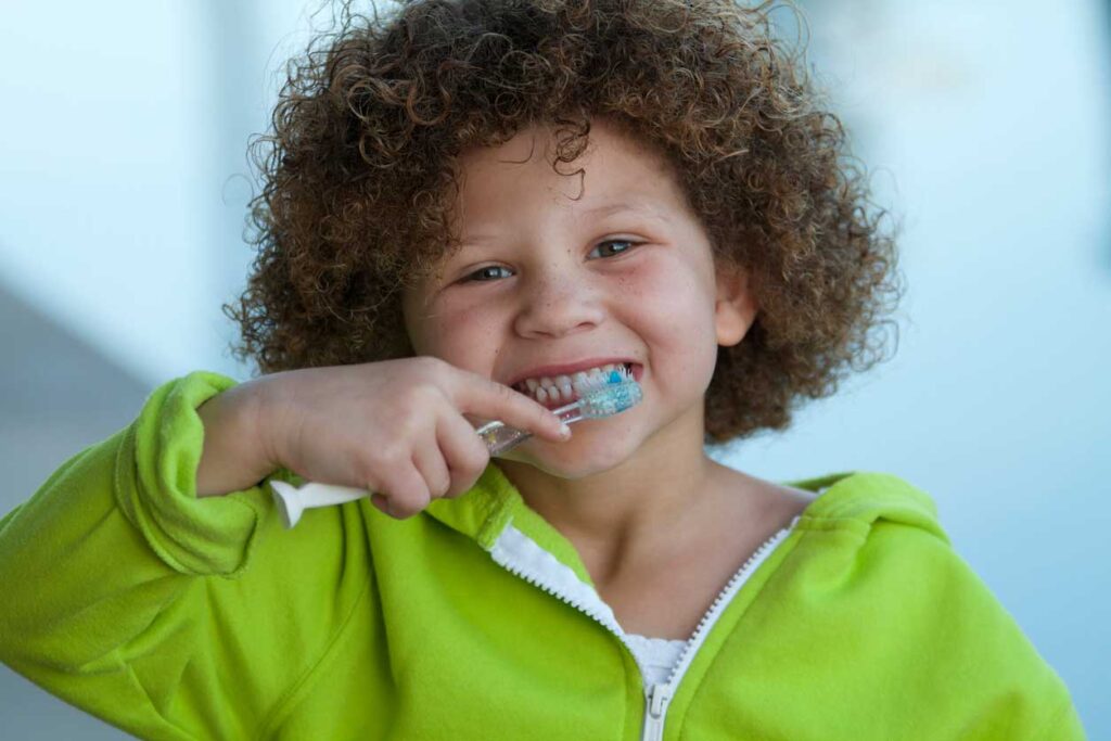 Little boy in neon green sweatshirt brushing his teeth.